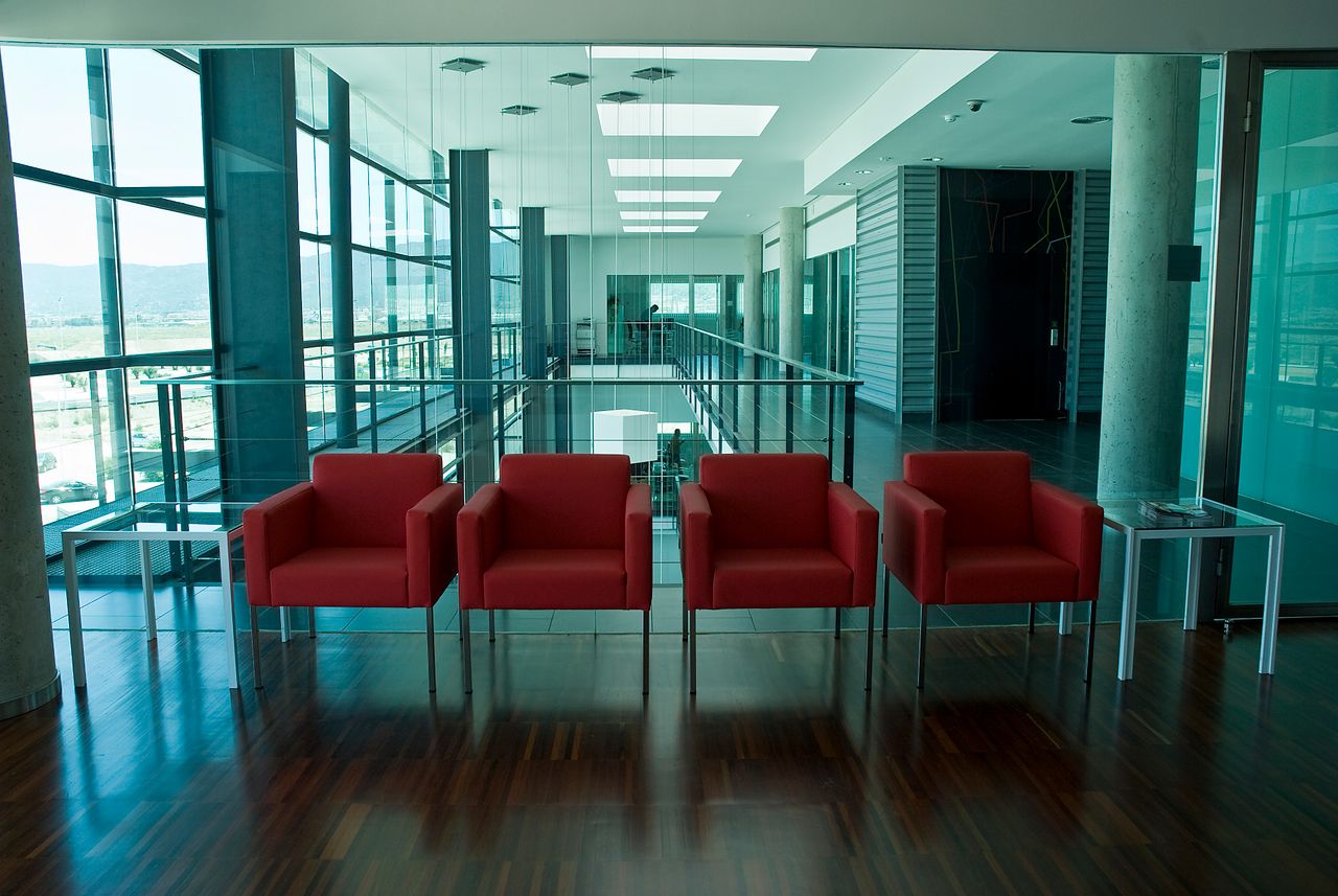 A spacious modern office lobby featuring bright red chairs and glass windows with abundant natural light.